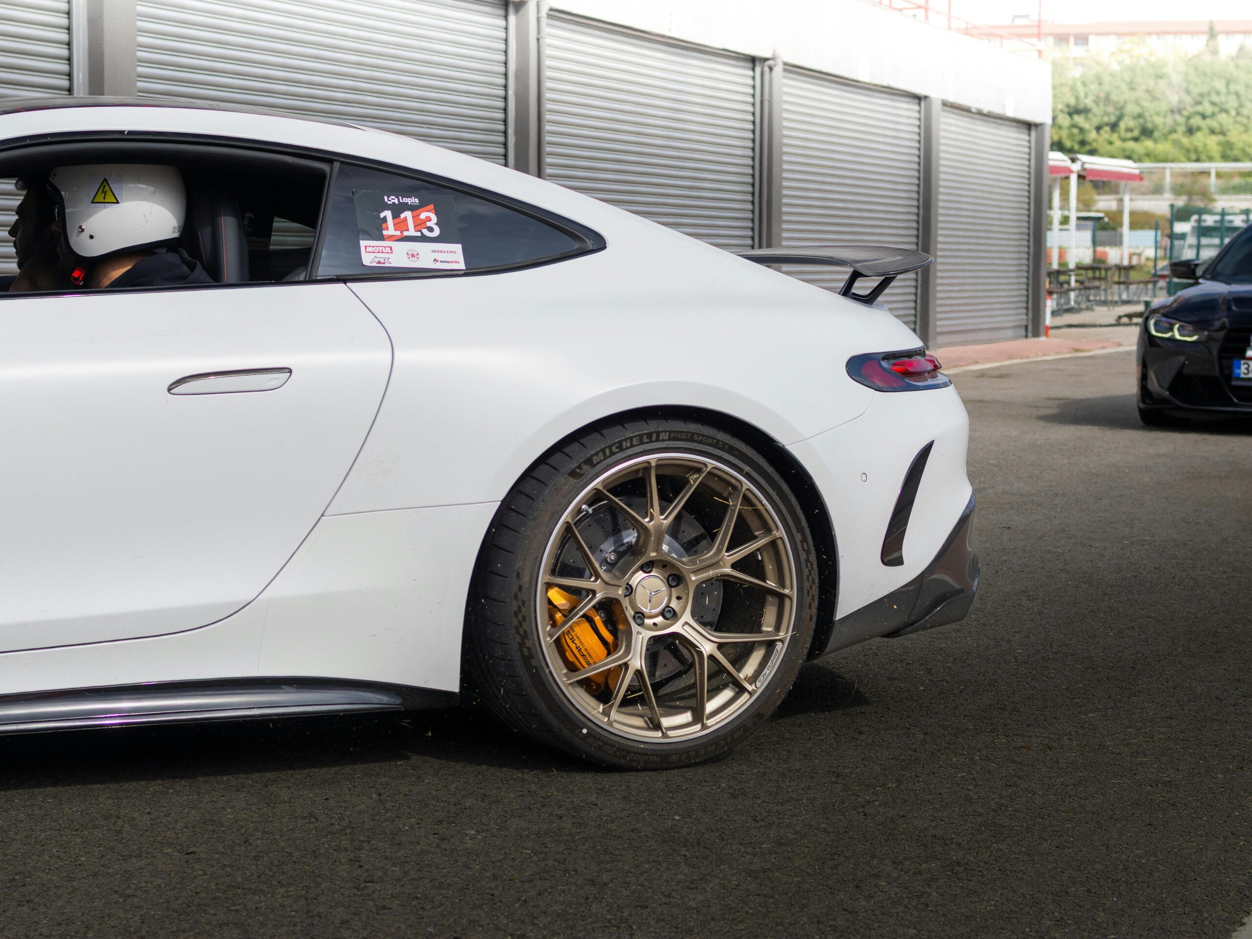 Close-up of a white sports car with helmeted driver on a race track.