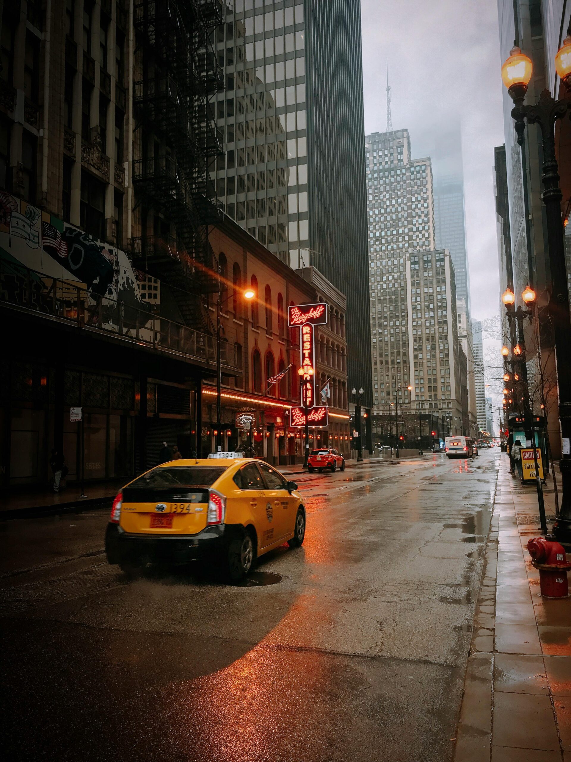 A yellow taxi navigates a rainy street in downtown Chicago, surrounded by towering skyscrapers.